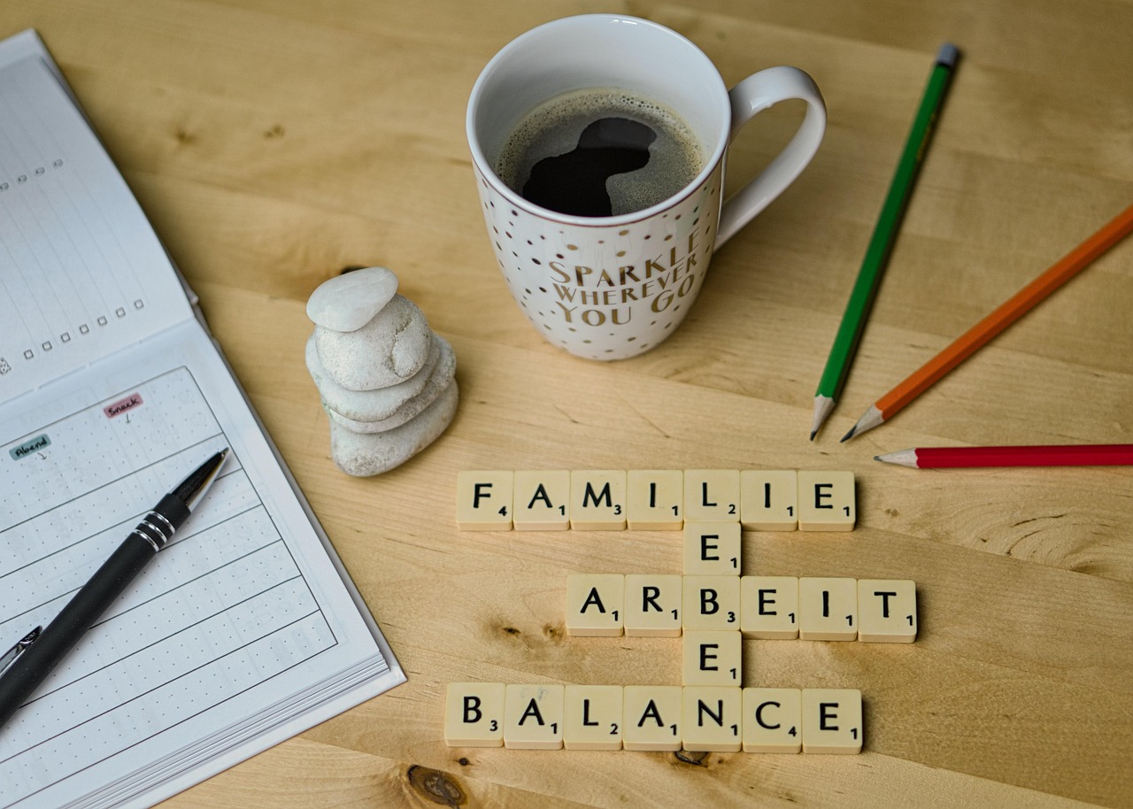 Image showing an office desk with a laptop and work papers, alongside coffee cups, coloring pens, and a family drawing, symbolizing the balance between work and personal life.